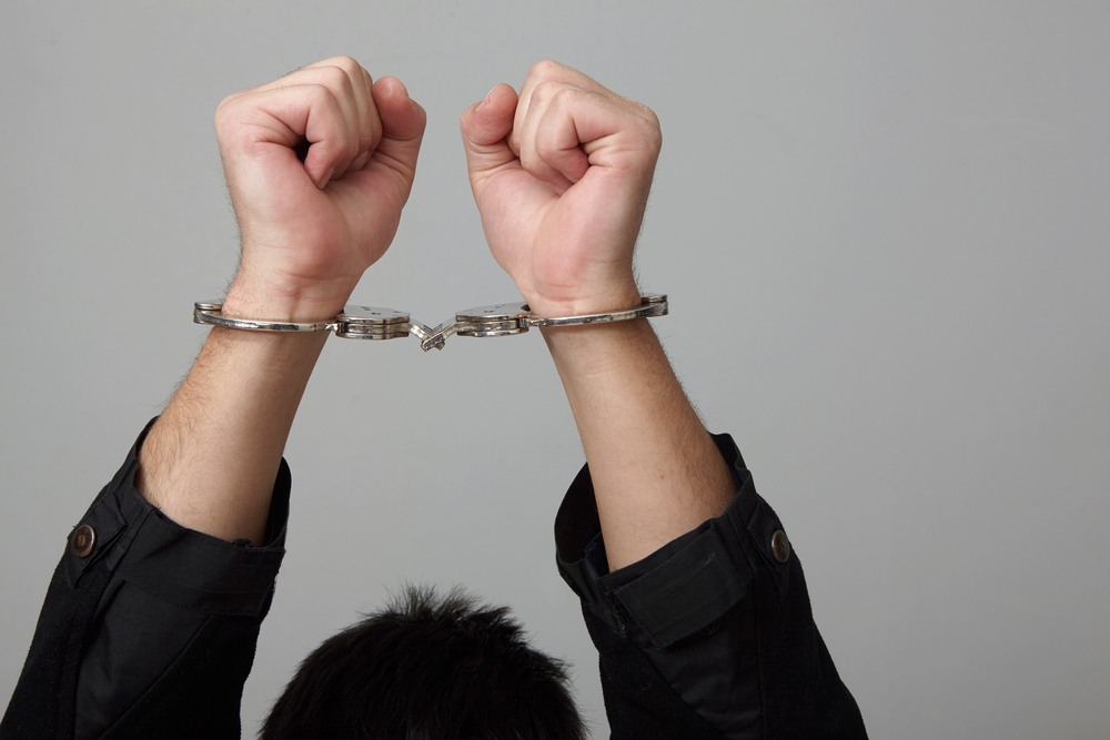 person wearing handcuffs, arms above their head