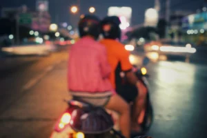 Two people ride on a scooter in the city at night.