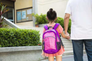 young girl wearing backpack holding dad's hand