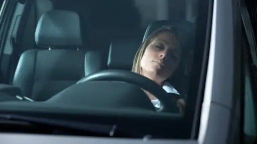 A woman sleeping in the driver’s seat of a car, suggesting the complexities of DUI laws regarding intoxication without active driving.