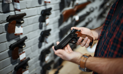 Man inspecting a gun in front of a display of firearms.