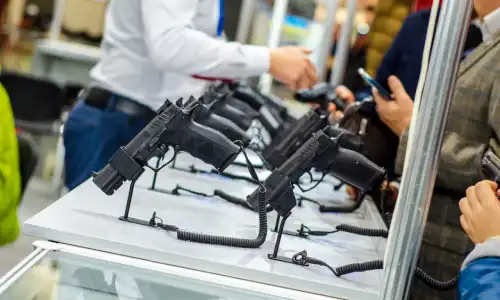 Firearms on display with people browsing in the background.